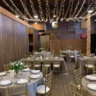 Decorated banquet hall with round tables, gold chairs, and string lights overhead