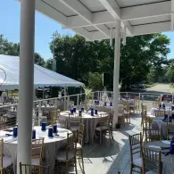 Outdoor event patio with round tables, gold chairs, and white tents under a covered pavilion.
