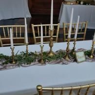 Brass candelabras lined up on a white tablecloth at a banquet setup