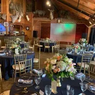 Banquet hall set for an elegant event, with round tables, floral centerpieces, and a lit projection screen