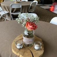 Small floral centerpiece with pink rose and candles on a wooden round table in a banquet hall