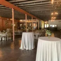 Elegant banquet hall with white-draped cocktail tables, chandeliers, and warm wooden decor