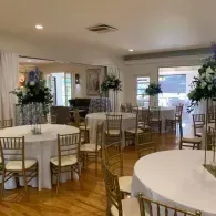 Elegant banquet hall with round tables, gold chairs, and potted plants on a wood floor