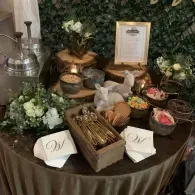 Buffet table with flowers, bowls of snacks, and a framed sign on a brown tablecloth