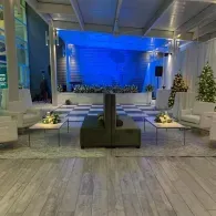 Modern lounge with white sofas, coffee tables, and a blue-lit stage in the background
