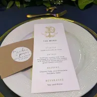 Wedding table setting with gold-rimmed plates, menu card, and brown place card on a dark tablecloth