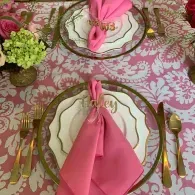 Elegant pink table setting with gold-rimmed plates, folded pink napkins, and gold cutlery on a floral tablecloth