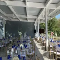 Outdoor event reception with round tables, gold chairs, and blue water bottles under a white canopy