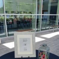 Outdoor sign near glass building entrance beside a cart of fruit and bottles