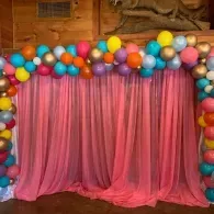 Pink curtain backdrop framed by colorful balloons in a festive party setup