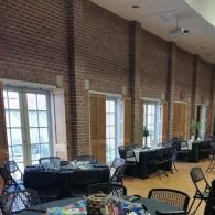 Empty brick-walled event room with windows, tables, and folding chairs near the wall