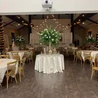 Elegant wedding reception hall with round tables, gold chairs, and a floral centerpiece on a white-clothed table