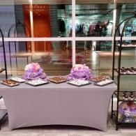 Buffet table with purple flower arrangements and trays of desserts in a lobby or event space