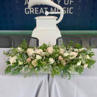 White decorative urn with cream floral arrangement on a stage table, in front of a blue backdrop