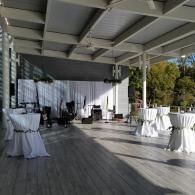 Covered outdoor event space with white-draped cocktail tables and a small stage backdrop