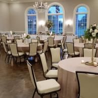 Elegant banquet hall with round tables, cream chairs, and blue-lit arched windows