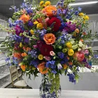 Vibrant mixed-flower bouquet in a glass vase, with orange, purple, yellow, and red blooms.