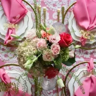 Pink floral arrangement with roses and greenery in a decorative white vase against a pink backdrop