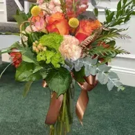 Colorful floral arrangement with orange, pink, and green flowers tied with brown ribbons in a glass vase