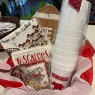 Gift basket with Tuscany-themed items, including a decorative platter, paper cups, and red tissue paper