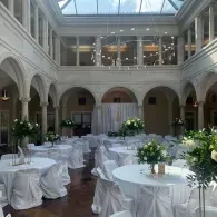 Elegant courtyard venue with white-draped tables, floral centerpieces, and arched walls under a glass skylight.
