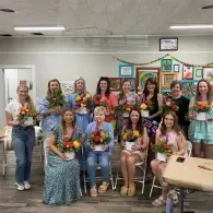 Group of people holding bouquets in a classroom, posing in front of colorful display boards.