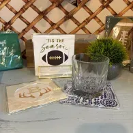 Decorative shelf with framed football sign, small succulent, coaster, and candle holders on a gray table.