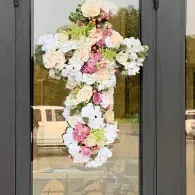 Floral cross decoration with white and pink flowers hanging on glass doors