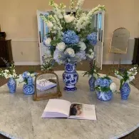 Blue and white floral arrangements on a table with an open book in a formal indoor setting