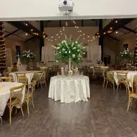 Decorated wedding reception hall with round tables, string lights, and a floral centerpiece on the front table