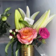 Mixed bouquet with pink, white, and green flowers in a gold vase against a gray background