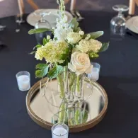 Floral centerpiece of white and pale green flowers in a glass vase on a mirrored tray at a formal table setting