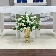 White floral arrangement in a gold vase centered beneath a white draped table