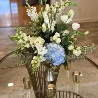 Floral arrangement with white flowers and a blue hydrangea in a glass vase on a table