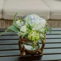 Blue and white floral arrangement in a decorative gold vase on a dark table outdoors