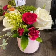 Pink vase of red and white roses with green filler flowers on a table