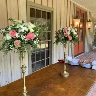 Wooden table with pink and white floral arrangements on gold stands in a porch hallway