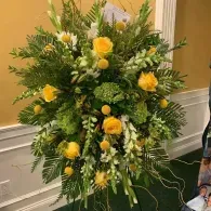 Yellow and white floral arrangement with greenery on an easel in an indoor setting