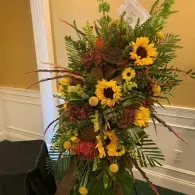 Tall floral arrangement with sunflowers, greenery, and autumn-colored flowers in an indoor setting
