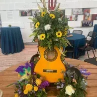 Guitar-shaped floral arrangement with yellow and white flowers displayed indoors on a wooden floor