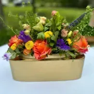 Colorful mixed flower arrangement in a beige rectangular planter against a blurred green background