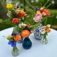 Three small glass vases holding colorful flowers on a white table outdoors