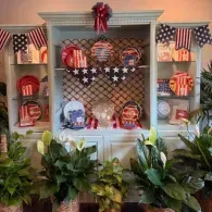 Patriotic display with red, white, and blue balloons, flags, and sports helmets above green plants