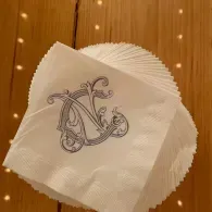 Stack of white napkins with a decorative monogram on a wooden table