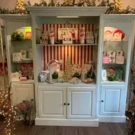 White hutch display with holiday decor, candles, greenery, and red-striped backing in a cozy room.