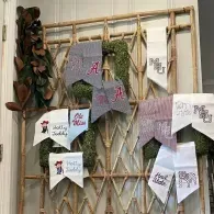Handmade textile samples and tags pinned on a wooden lattice display, with leaves hanging on the left.
