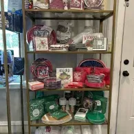Glass cabinet displaying neatly arranged red, green, and white boxed gift sets and tableware