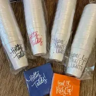 Assorted tumblers with “together faith” and “good vibes” designs in white, blue, and orange on burlap background