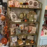 Shelf of autumn-themed decorative figurines, framed art, and small ornaments in a shop display.