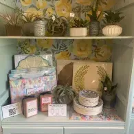 Pastel floral shelves with potted plants, gift boxes, and decorative trays on a white cabinet